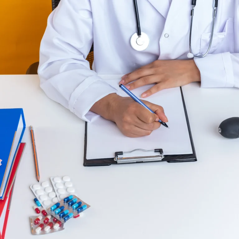 young-female-doctor-wearing-medical-robe-with-stethoscope-sits-table-with-medical-tools-writing-something-clipboard-isolated-yellow-background